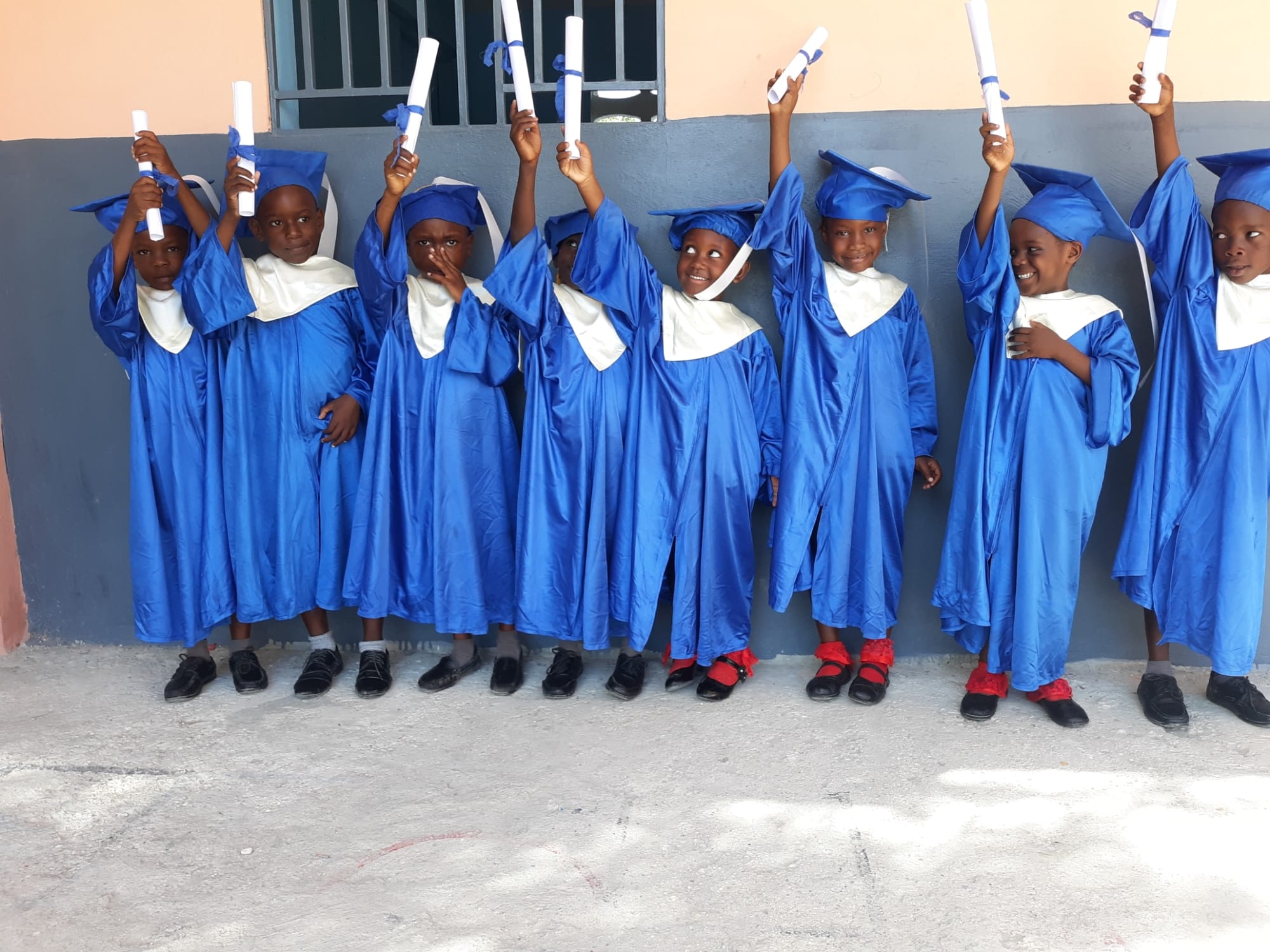 CFAM children celebrating graduation in blue gowns and holding their certificates