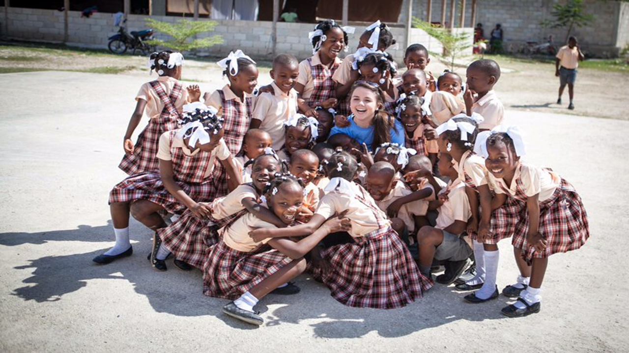 A group of smiling schoolchildren gathered with a visitor